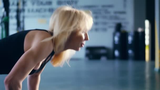 Close-up, portret, aantrekkelijke blonde vrouw in zwarte top, doet push ups met stromende haren, voert oefeningen in de sportschool. — Stockvideo