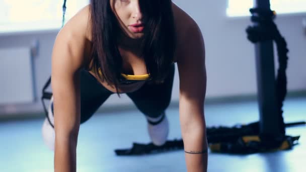 Primer plano, retrato, atractiva mujer morena en polainas, top amarillo y zapatillas de deporte realiza ejercicios en bucles TRX, correas en el gimnasio. bonita mujer con hermoso, deportivo, cuerpo tonificado entra para — Vídeos de Stock