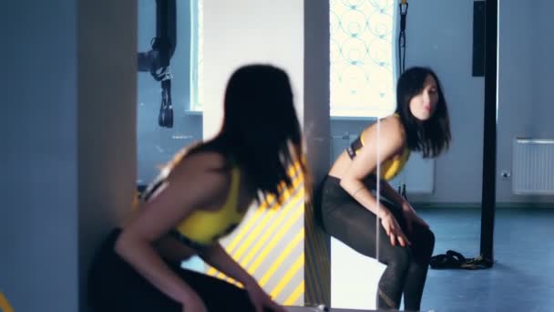 Brune jolie femme au corps attrayant, en leggings, haut jaune et baskets, se penche en dansant devant le miroir. elle se déplace très excitamment — Video