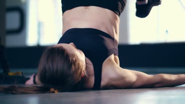 Attraktiv blond kvinna i svarta leggings, topp och sneakers utför övningar på Trx loopar, remmar, liggande på golvet i gymmet. — Stockvideo