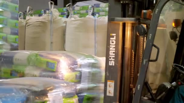 UKRAINE, CHERKASY, 25 de março de 2019: empresa agrícola MAIS. Motorista de empilhadeira empilhando paletes de pacote grande de milho com pelo carregador de empilhador, leva paletes, transporta-os de um grande armazém . — Vídeo de Stock