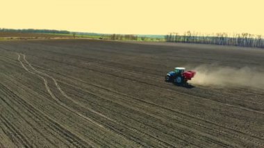 Büyük tekerlekler üzerinde tarım traktörü havadan görünümü verimli çiftlik alanı boyunca sürmek, tohum matkap ile mineral gübre yayılan, sürülmüş zemin üzerinde büyük toz yükseltir. Bahar toprak ekimi