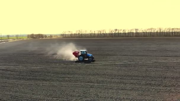 Vue aérienne du tracteur agricole sur de grandes roues parcourt le champ fertile de la ferme, épandant des engrais minéraux avec semoir, soulève une grande poussière sur le sol labouré. Culture printanière du sol — Video