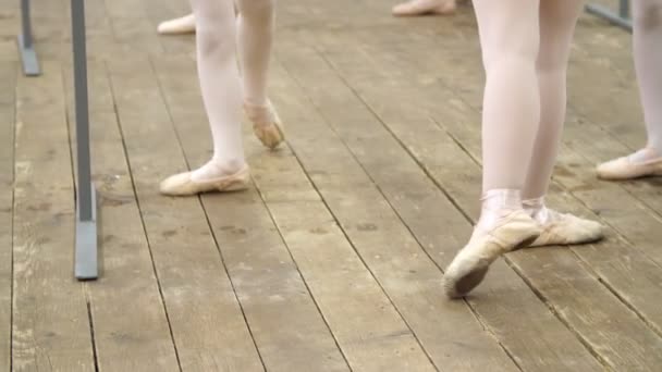 Крупный план, юные ноги балерины в балетных туфлях, пуантах, в бежевых трико, выполнять упражнения рядом с баром, на старом деревянном полу в балетной школе, во время урока балета — стоковое видео