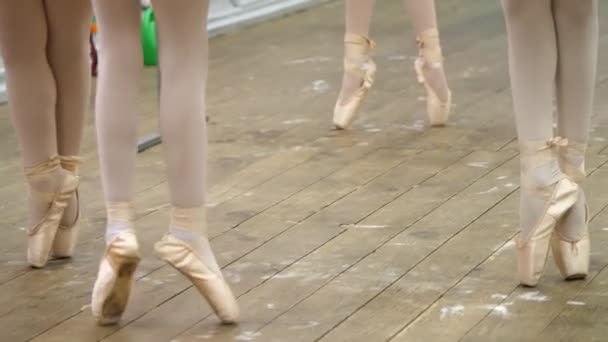 Closeup , Young ballerina legs in ballet shoes, pointes, in beige leotards, perform exercises near barre, on an old wooden floor in a ballet school, during ballet lesson — Stock Video