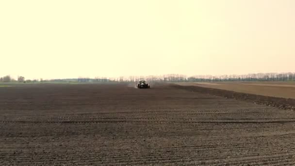 levé aérien, un gros tracteur traverse un champ labouré de terre noire, soulevant un nuage de poussière derrière lui. saison de plantation. plantant des pommes de terre. beau jour de printemps 