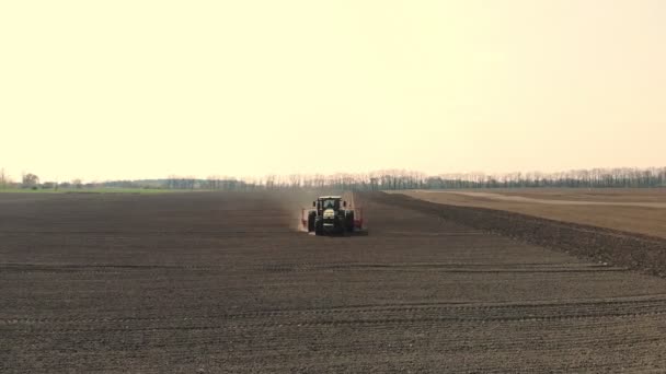 空中勘察时，一辆大型拖拉机穿过一片被犁开的黑土，身后扬起一团尘土。种植季节。种植土豆。美好的春天 — 图库视频影像