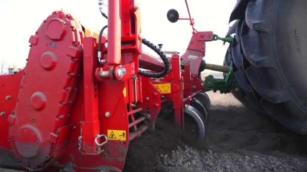 クローズアップ、機械加工ポテトの植え付けのプロセス。特別な装置が付いている大きいトラクターは耕された黒い土の分野で新しく植えられたジャガイモのための長い平らな上の列、毛皮、マウンドを作る、春 — ストック動画