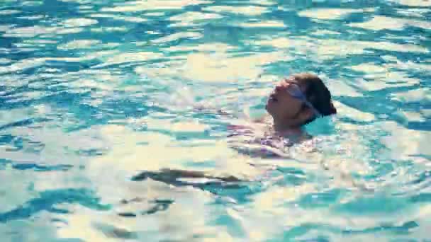 Menina nada na piscina na parte de trás, em óculos especiais para a piscina, óculos de natação — Vídeo de Stock