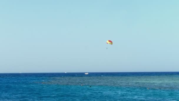 Fallschirm vom Kitesurfen schwebt über dem Wasser Kante gegen den klaren blauen Himmel. Sommer, Seelandschaft. Wasseroberfläche, ruhiges türkisfarbenes Meer und blauer Himmel. Urlauber schwimmen mit Masken zum Schnorcheln — Stockvideo
