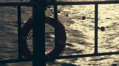 yakın çekim, gün batımında deniz dalgaları, yumuşak güneş ışığı ışınları. su üzerinde parlama. pantone, iskele asılı bir cankurtaran şamandırası ana hatlarıyla. tatilciler denizde şnorkel için maskeleri ile yüzmek.