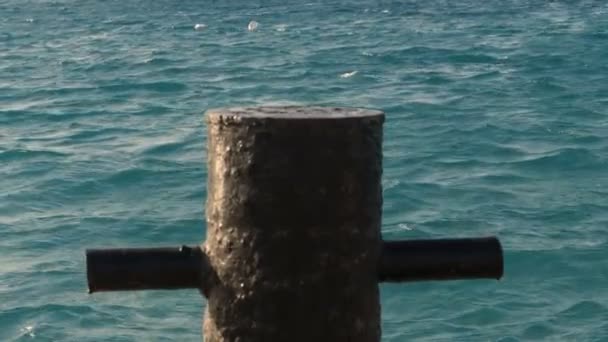 Close-up, oude metalen roestige aanmeren Bolder is een kleine paal op de pier waarop het schip is vastgemaakt, een jacht met touwen en kabels. op de achtergrond van de zee. — Stockvideo