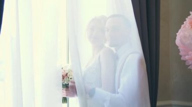 gelin ve damat perde arkasında öpücük, pencerenin yanında.