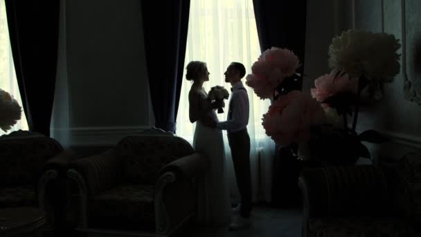 Contornos escuros da noiva e noivo em frente à janela. A rapariga e o rapaz estão de pé, de frente um para o outro e a falar. casamento — Vídeo de Stock