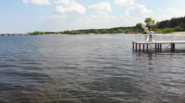 hava video, güzel yeni evli çift, gelin ve damat açık havada dans, güzel bir iskelede, mavi deniz ve gökyüzüne karşı. damat elinde balonları tutar, yaz güneşli bir gün. Düğün