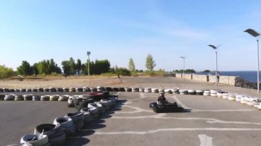 Gençler açık havada araba yarışı yapıyor. Eski tekerleklerden yapılmış güvenlik bariyerleri var. On yaşında bir kız go-kart kullanıyor. Go-kart yarışı. Yaz