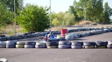 Gençler açık havada araba yarışı yapıyor. Eski tekerleklerden yapılmış güvenlik bariyerleri var. On yaşında bir kız go-kart kullanıyor. Go-kart yarışı. Yaz