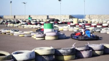 Gençler açık havada araba yarışı yapıyor. Eski tekerleklerden yapılmış güvenlik bariyerleri var. On yaşında bir kız go-kart kullanıyor. Go-kart yarışı. Yaz