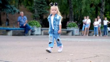 Şık bir kostüm ve kafasında at kuyruğu olan küçük bir kız parkta yürüyor..