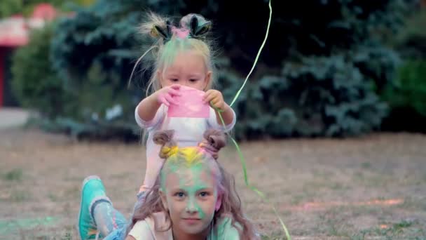 Dos niñas hermanas, una adolescente y una pequeña yacen en el césped, jugar y espolvorear con arena de colores en un parque , — Vídeos de Stock