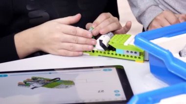 Öğrenciler, tabletteki çizimlere göre tasarımcıyı kullanarak bir cihaz oluşturuyorlar. Robot Bilimi Okulu, Kök Eğitimi