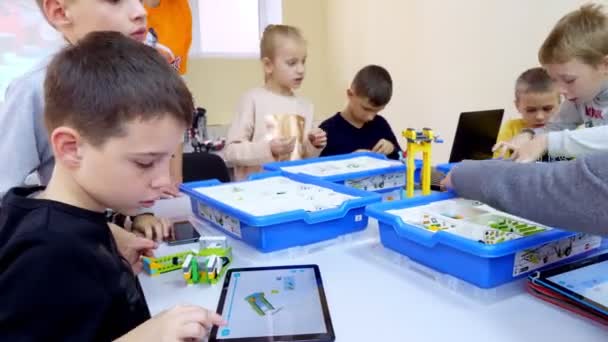 Estudantes, crianças, meninos e meninas, criar dispositivos usando o designer, peças não ferrosas, blocos, de acordo com desenhos em instruções em tablets. Escola de Robótica, educação STEM . — Vídeo de Stock