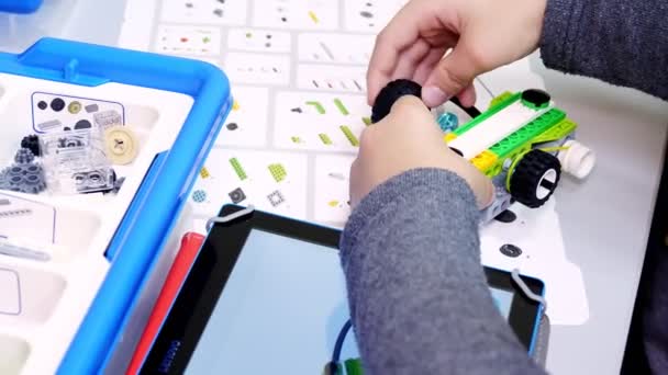 Close-up, student maakt apparaat, machine, met behulp van de ontwerper, volgens de tekeningen in de instructie op de tablet. School of Robotics, Stamonderwijs — Stockvideo