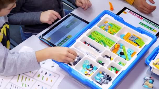 Close-up, students create devices, machines, using designer, small color details, according to the instruction on the tablet . School of Robotics, STEM education — Stock Video