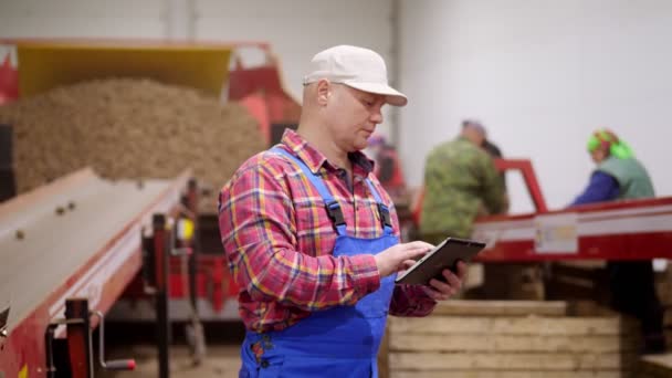 Agricultor monitorar a qualidade das batatas com tablet digital, na classificação de correia transportadora em armazém de armazenamento de batata. colheita de batata, agricultura, agricultura, indústria alimentar . — Vídeo de Stock