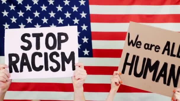 I manifestanti tengono striscioni con slogan - Stop al razzismo. Siamo TUTTI UMANI - sullo sfondo della bandiera USA. Lotta contro il razzismo, per la parità dei diritti negli Stati Uniti . — Video Stock