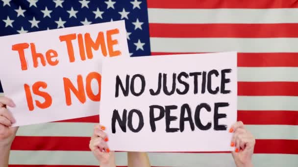 Manifestantes sostienen pancartas con eslóganes - El momento es ahora. NO JUSTICIA NO PAZ - en el contexto de la bandera de Estados Unidos. Lucha contra el racismo, por la igualdad de derechos en Estados Unidos . — Vídeos de Stock