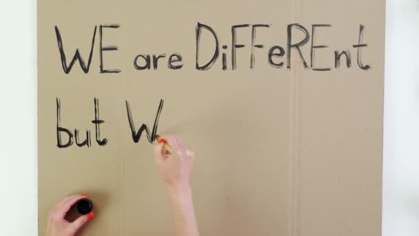 Timelapse. close-up, hand writes slogan, with brush, using black paint on cardboard banner. We are different, but we are equal in our rights. Fighting against racism in USA. — Stock Video