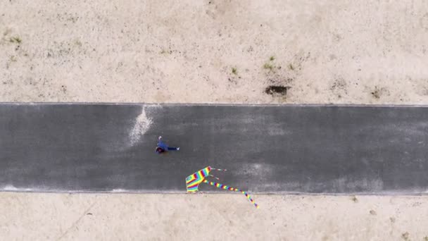 Aéro. vue de dessus. une fille volant un cerf-volant arc-en-ciel lumineux et coloré dans le ciel sur la plage. beau temps, jour du printemps. lancement de cerf-volant. Activités de plein air amusantes . — Video