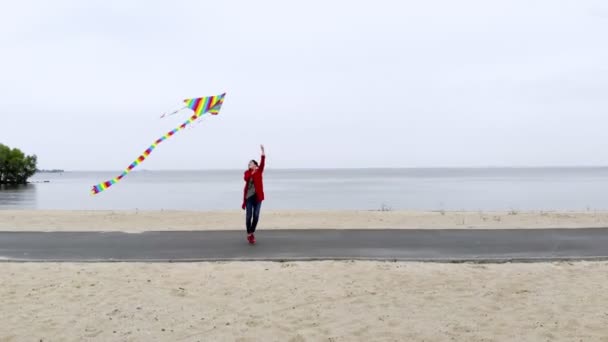 Luchtvaart. vrouw vliegt een heldere, kleurrijke regenboog vlieger in de lucht op het strand. mooi weer, lentedag. vliegende vlieger lancering. Leuke buitenactiviteiten. — Stockvideo