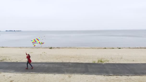 Aero. kobieta leci jasnym, kolorowym latawcem tęczowym w niebo na plaży. Ładna pogoda, wiosenny dzień. odpalanie latawca. Zabawa na świeżym powietrzu. — Wideo stockowe