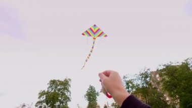 Yakın plan, adam mavi gökyüzüne parlak, renkli bir gökkuşağı uçurtması fırlatıyor. Güzel hava, bahar günü. Uçurtma fırlatılıyor. Eğlenceli açık hava aktivitesi.