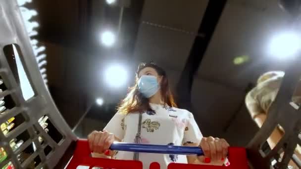 女性,使い捨て医療マスクを身に着けているとコロナウイルス肺炎の発生中にスーパーマーケットで買い物.流行時間中の保護と対策. — ストック動画