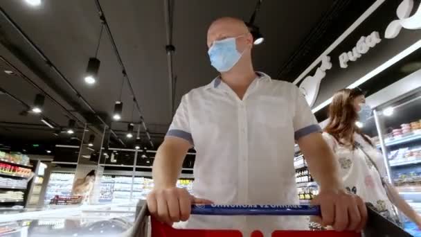 CHERKASY, UCRANIA, 4 de junio de 2020: Hombre, con máscara médica desechable y compras en el supermercado durante el brote de neumonía por coronavirus . — Vídeo de stock