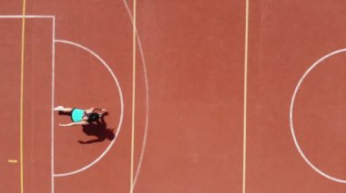 Aero, en iyi manzara, spor giyim sektöründe spor yapan kadın çeşitli egzersizler yapıyor. Beyaz işaretli turuncu basketbol sahasının arka planı. Açık hava sporları. Online eğitim. Yaz günü. Stadyumda.