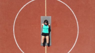 Aero, en iyi manzara, spor giyim sektöründe spor yapan kadın çeşitli egzersizler yapıyor. Beyaz işaretli turuncu basketbol sahasının arka planı. Açık hava sporları. Online eğitim. Yaz günü. Stadyumda.