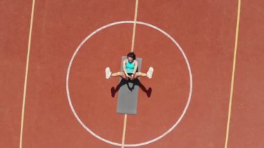 Aero, en iyi manzara, spor giyim sektöründe spor yapan kadın çeşitli egzersizler yapıyor. Beyaz işaretli turuncu basketbol sahasının arka planı. Açık hava sporları. Online eğitim. Yaz günü. Stadyumda.