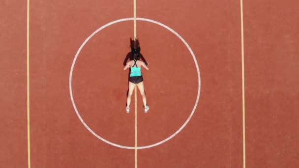 Aero, bovenaanzicht, Fitness vrouw in sportkleding die verschillende oefeningen doet. achtergrond van oranje basketbalveld met witte markeringen. Buitensporten. online opleiding. Zomer dag. in het stadion — Stockvideo