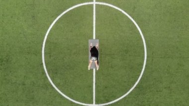 Aero, top view, spor giyimli kadın spor minder üzerinde çeşitli egzersizler yapıyor, yeşil futbol sahasında, stadyumda beyaz işaretli. Açık hava sporları. Online eğitim. Sıcak yaz günü. sağlıklı