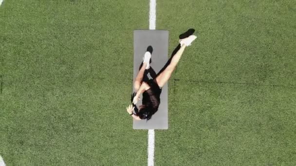 Aero, top view, Fitness woman in sportswear doing various exercises on sports mat, on green football field with white markings, at stadium. Outdoor sports. online training. hot summer day. healthy — Stock Video