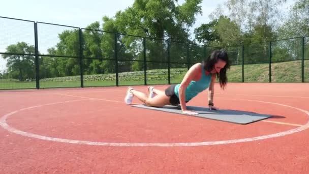 Femme de fitness en vêtements de sport faisant divers exercices sur tapis de sport, sur un terrain de basket-ball orange avec des marques blanches, au stade. Sports de plein air. formation en ligne. jour d'été. — Video