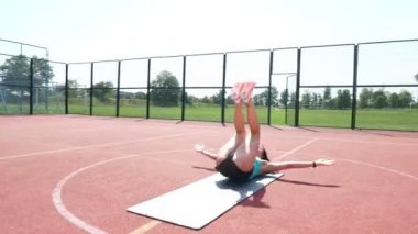 Spor giyim bölümünde spor ayakkabılı bir kadın stadyumdaki turuncu bir basketbol sahasında spor minderi üzerinde çeşitli egzersizler yapıyor. Açık hava sporları. Online eğitim. yaz günü.