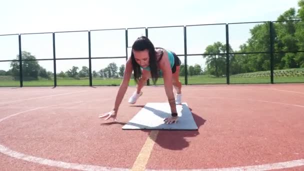 Fitnessvrouw in sportkleding die verschillende oefeningen doet op sportmat, op een oranje basketbalveld met witte markeringen, in het stadion. Buitensporten. online opleiding. zomerdag. — Stockvideo