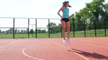 Spor kıyafetli kadın, stadyumdaki beyaz işaretli turuncu bir basketbol sahasında çeşitli egzersizler yapıyor. Açık hava sporları. Online eğitim. yaz günü.