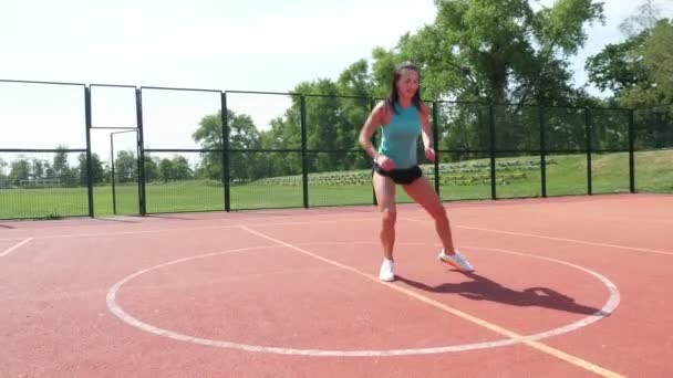 Wanita fit dalam pakaian olahraga melakukan berbagai latihan di lapangan basket oranye dengan tanda putih, di stadion. Olahraga luar ruangan. Pelatihan online. Hari musim panas. — Stok Video