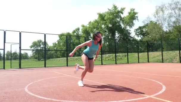 Фітнес-леді в спортивному одязі роблять різні вправи на помаранчевому баскетбольному полі з білими позначками, на стадіоні. Спорт на відкритому повітрі. онлайн-тренінги. літній день . — стокове відео